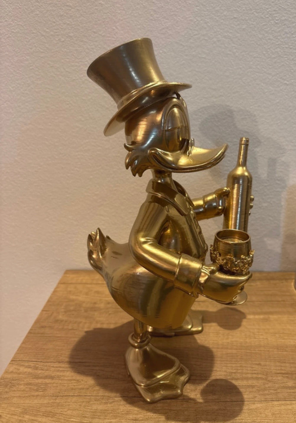 Dagobert Duck Statue mit Glas Wein und Flasche