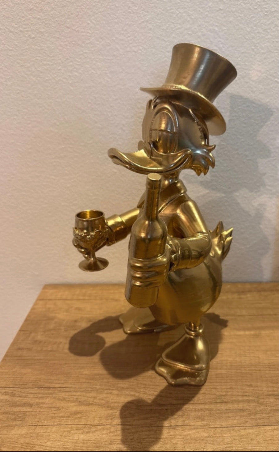 Dagobert Duck Statue mit Glas Wein und Flasche